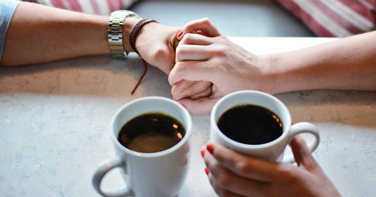 カフェでコーヒーを飲みながら手を繋ぐカップル